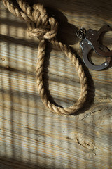 Rope with knot and handcuffs on a wooden surface.