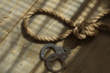 Rope with knot and handcuffs on a wooden surface.