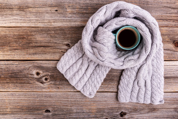 Obraz na płótnie Canvas A winter scarf on wooden table wraps a cup of tea or coffee.