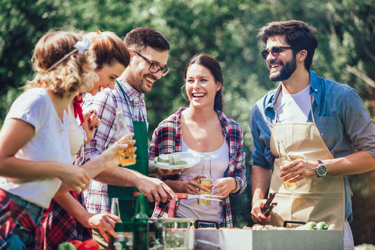 Young friends having fun grilling meat enjoying barbecue party.