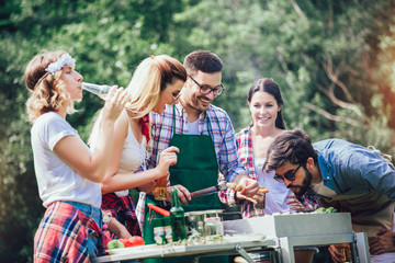 Young friends having fun grilling meat enjoying barbecue party.