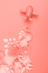 Travel concept with wood plane and paper flowers, petals on pink background.