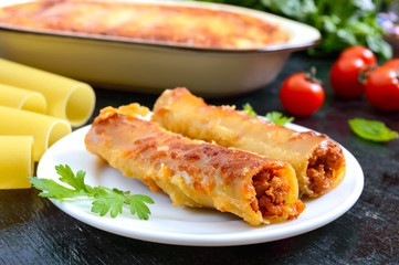 Stuffed cannelloni with bechamel sauce. Cannelloni pasta baked with meat, cream sauce, cheese on a black background