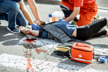 Ambluence workers applying emergency care to the injured bleeding man lying on the pedestrian crossing after the road accident