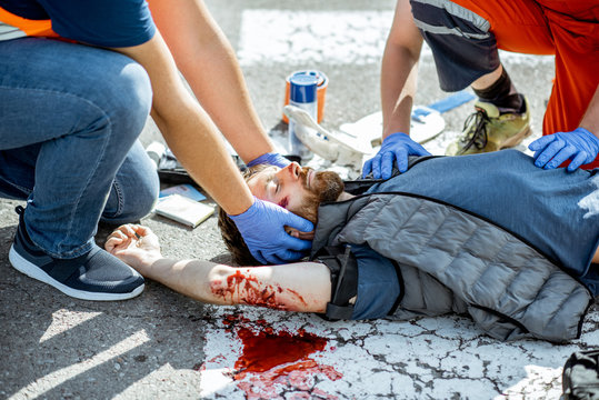 Ambluence workers applying emergency care to the injured bleeding man lying on the pedestrian crossing after the road accident
