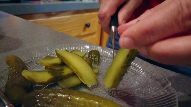 Women cutting green pickles into thin slices in a kitchen.