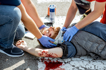 Ambluence workers applying emergency care to the injured bleeding man lying on the pedestrian...