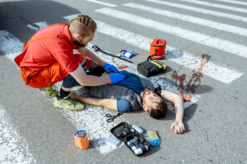 Ambluence worker applying emergency care to the injured bleeding man lying on the pedestrian...