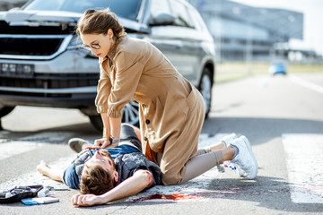 Woman making artificial respiration to the injured bleeding man lying on the pedestrian crossing...