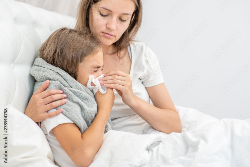 Wall mural young mother at home blowing the nose of her little girl