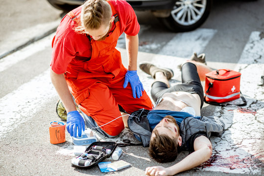 Ambluence worker applying emergency care with defibrillator to the injured bleeding man lying on the pedestrian crossing