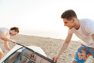Fototapeta premium Two happy men building a tent at the beach
