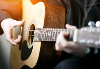 The guitarist in black clothes, illuminated by bright orange light, plays a beautiful melody on a wooden acoustic six-string guitar