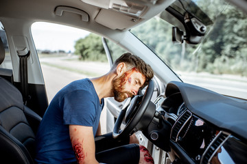 Fototapeta na wymiar Injured man with a broken head and bleeding wounds sitting on the driver seat without consciousness after the road accident inside the car
