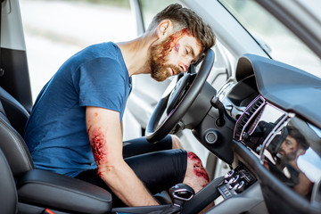 Injured man with a broken head and bleeding wounds sitting on the driver seat without consciousness...