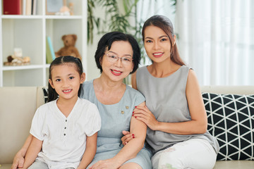 Portrait of Asian family generation sitting on sofa and smiling at camera together in living room at home