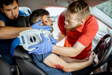 Medics wearing neck corset to an injured man sitting in the car after the road accident, providing...