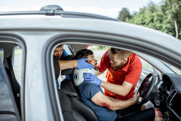 Medics wearing neck corset to an injured man sitting in the car after the road accident, providing...