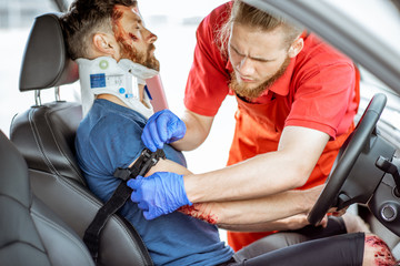 Medic wearing tourniquet on arm of injured person sitting on the driver saet after the road...