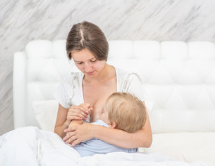 Mother breastfeeding her baby at home on the bed. Empty space for text