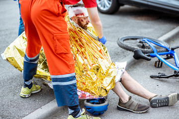 Ambluence worker covering injured man with thermal blanket, providing emergency care after the road...