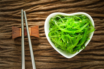 Hiyashi Wakame Chuka or seaweed salad in white heart bowl  with stainless steel chopsticks on wooden table, Japanese food