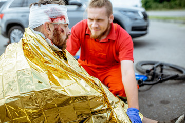 Ambluence worker covering injured man with thermal blanket, providing emergency care after the road...