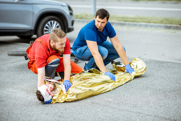 Ambluence workers covering injured man with thermal blanket, providing emergency care after the road accident