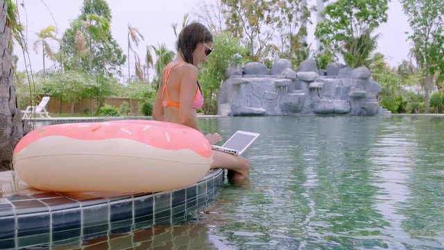 A young woman sits by the pool with minicomputer. selective focus