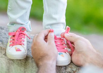 Close up father helping her little daughter to tie shoelaces on summer day