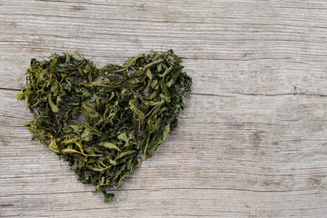Fototapeta na wymiar Large Heart Of Dried Cannabis Leaf Or Marijuana On Rustic Wooden Table Surface. Rasta Background.
