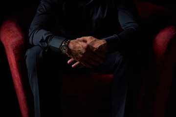 male businessman in a black suit sitting in red chair, black background, no faces visible, studio...