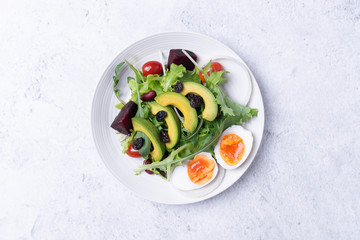 Fresh healthy vegetable salad with egg, tomato, avocado, spinach, lettuce in plate on table background.
