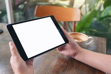 Mockup image of a woman holding black tablet pc with blank with coffee cup on wooden table