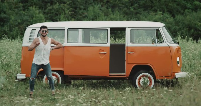 Charismatic guy dacing professional in front of a retro van , in the middle of nature. 4k
