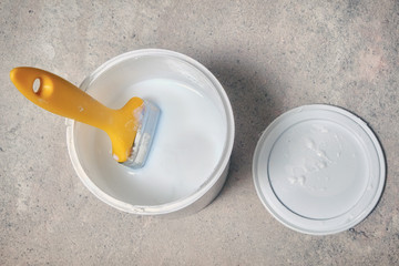 Yellow brush over a bucket of white paint. A jar of white enamel stands on the concrete floor. Carrying out painting of walls in new housing.