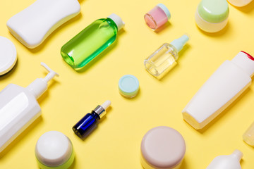 Composition of different sized cosmetic jars and bottles on yellow background. Beauty care concept with copy space