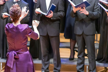 A young girl in dress conducts a male choir