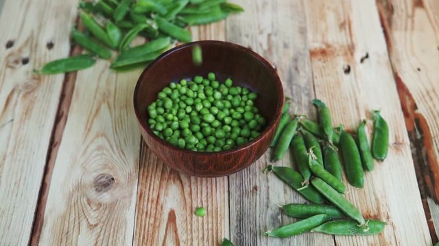 closeup of woman hand depod green peas in brown dish, on wooden table.