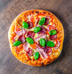 Pizza with Mozzarella cheese, ham, tomato sauce, salami, onion, pepper, Spices and Fresh basil. Italian pizza on wooden table background