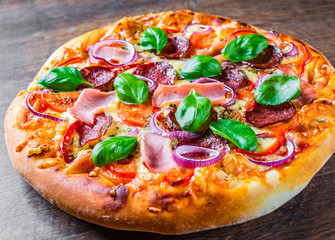 Pizza with Mozzarella cheese, ham, tomato sauce, salami, onion, pepper, Spices and Fresh basil. Italian pizza on wooden table background