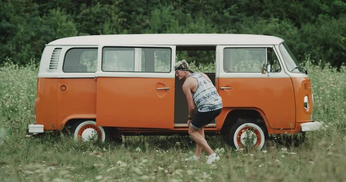 Stylish guy with sunglasses dancing amazing in front of retro van in the middle of nature