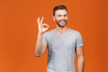 Portrait of a cheerful young man showing okay gesture isolated on the orange background. Ok sign.