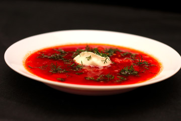 Bowl of beet root soup borscht with sour cream and greens isolated on black canvas with dark background