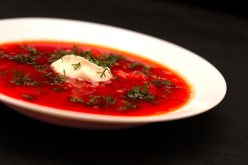 Bowl of beet root soup borscht with sour cream and greens isolated on black canvas with dark background
