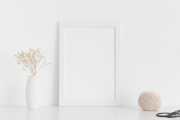 White frame mockup with workspace accessories  and gypshophila in a vase on a white table.Portrait...