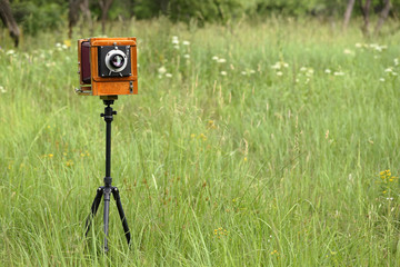 Vintage wooden large format film camera on a sunny meadow with green grass. The old studio camera for using glass plates.