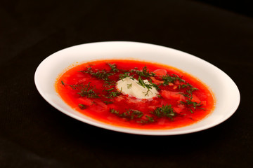 Bowl of beet root soup borscht with sour cream and greens isolated on black canvas with dark background