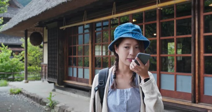 Woman send audio message on cellphone with the background of the Japanese wooden house