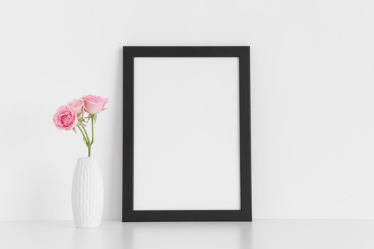 Black frame mockup with pink roses in a vase on a white table.Portrait orientation.